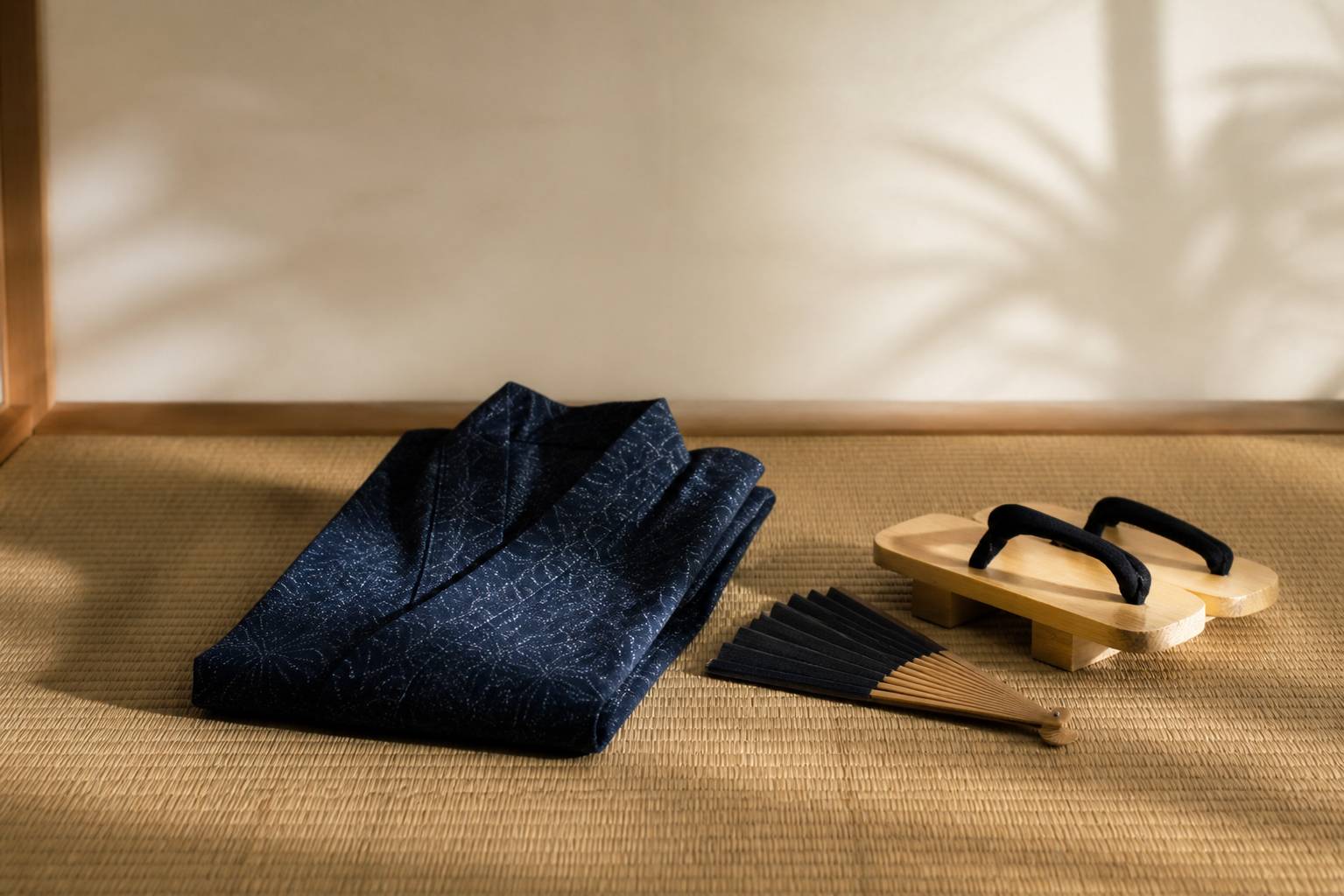 Yukata en coton indigo plié sur un tatami avec éventail plié et sandales geta en bois